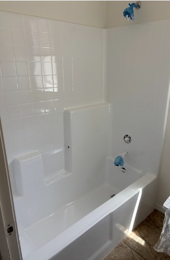 Completed senior access conversion: white refinished tub and tile surround with a built-in seat, fixtures still taped from the fresh finish